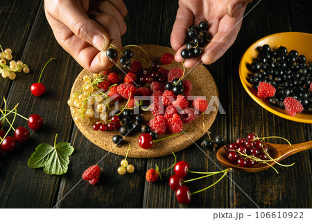 Many different fresh berries on the kitchen table and wooden stand. Hands of a man sorting blackcurrant before preparing fruit drink or compote in a restaurant Many different fresh berries on the kitchen table and wooden stand. Hands of a man sorting blackcurrant before preparing fruit drink or compote in a restaurant 106610922