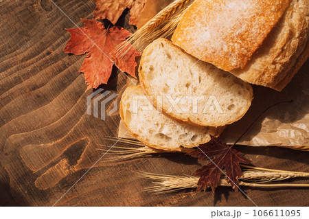 Sliced fresh loaf of bread in paper packaging with ears of wheat and maple leaves on a wooden table 106611095