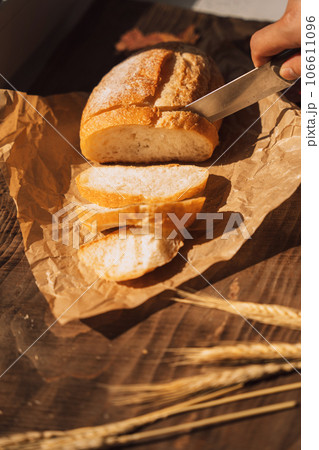 Sliced fresh loaf of bread in paper packaging with ears of wheat on a wooden table 106611096