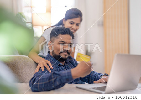 Happy smile couple Indian making online purchase on laptop by using credit card at home concept of shopping, bill payment and internet banking Happy smile couple Indian making online purchase on laptop by using credit card at home concept of shopping, bill payment and internet banking 106612318