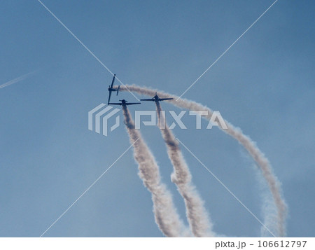 Three aircraft perform aerobatics, behind them stretches clearly visible against the blue sky inversion trail indicating the flight path. 106612797