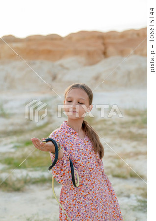 A teenage girl plays with a snake, holding it in her hands. Children and snake in the wild 106615144