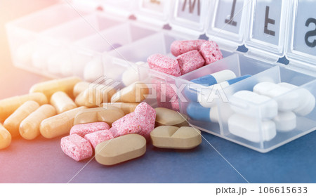 Weekly pill organizer or daily medicine pill box on blue background in bright sun rays. 106615633