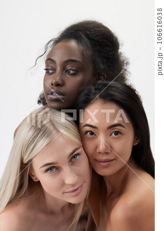Portrait of beautiful young african, caucasian and asian women with well-kept skin looking at camera against white background 106616038