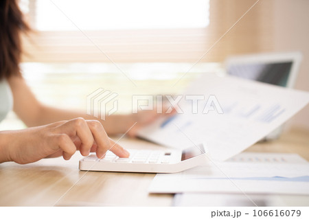 Asian woman working at home, Press the calculator to calculate the income - expenses of the house and use the laptop to record the information and check the accuracy, Home lifestyle. Asian woman working at home, Press the calculator to calculate the income - expenses of the house and use the laptop to record the information and check the accuracy, Home lifestyle. 106616079