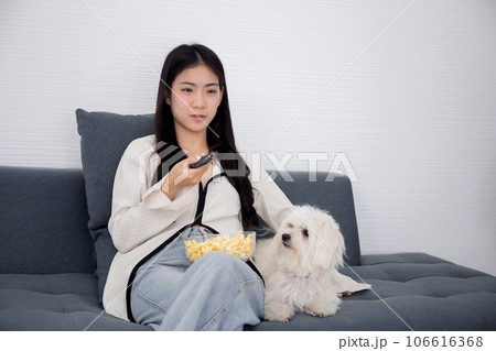 Beautiful young asian woman and dog sitting on sofa watching movie on television for leisure. 106616368