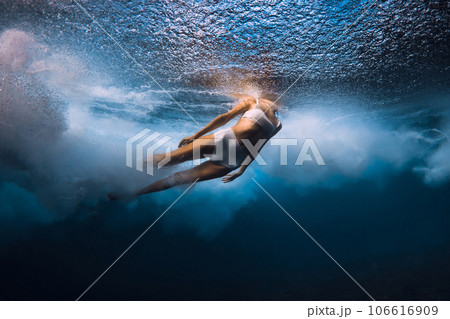 Woman dive under wave. Duck dive under crashing barrel wave in transparent ocean Woman dive under wave. Duck dive under crashing barrel wave in transparent ocean 106616909