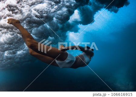 Woman dive under wave. Duck dive under crashing barrel wave in transparent ocean Woman dive under wave. Duck dive under crashing barrel wave in transparent ocean 106616915