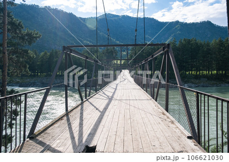 A wooden bridge with metal supports across a raging river in the Altai Mountains. Old broken bridge A wooden bridge with metal supports across a raging river in the Altai Mountains. Old broken bridge 106621030