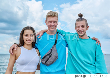 Portrait of cheerful teenage friends hugging on beach 106621388