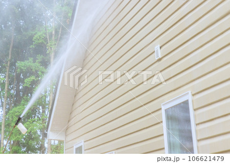Using high pressure nozzles, service worker efficiently washes siding houses with water soap cleaner 106621479