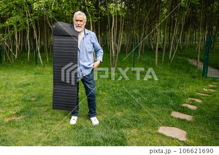 Senior man holding solar panel on in green yard. 106621690