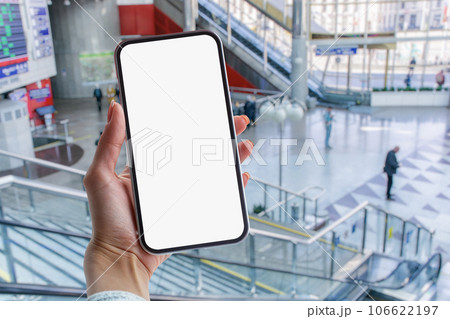 Girl holds in her hands a mock-up of a smartphone with a white screen against the background of a supermarket. 106622197