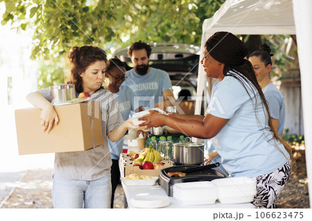 Diverse group of volunteers happily distributing food to the needy. Smiles and genuine happiness all around as they provide donations to homeless individuals and seniors facing poverty. Diverse group of volunteers happily distributing food to the needy. Smiles and genuine happiness all around as they provide donations to homeless individuals and seniors facing poverty. 106623475