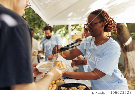 Detailed image of black woman at a food drive sharing free warm meals to poor caucasian homeless person. At local center group of volunteers feed and support the hungry and underprivileged. Detailed image of black woman at a food drive sharing free warm meals to poor caucasian homeless person. At local center group of volunteers feed and support the hungry and underprivileged. 106623528