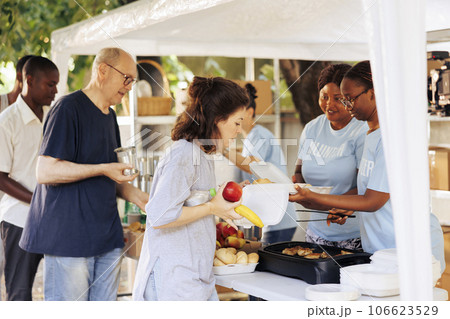 Compassionate volunteers distribute free food and provide humanitarian aid to the needy. Poor and homeless people of different ethnicities receiving nourishments from the non-profit organization. Compassionate volunteers distribute free food and provide humanitarian aid to the needy. Poor and homeless people of different ethnicities receiving nourishments from the non-profit organization. 106623529