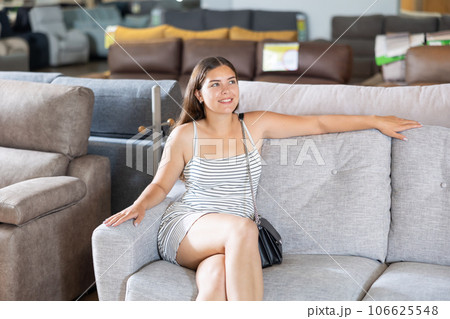 In furniture store,young girl is sitting on sofa with ottoman 106625548