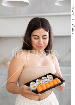 Smiling young woman holding sushi in the kitchen Smiling young woman holding sushi in the kitchen 106625652