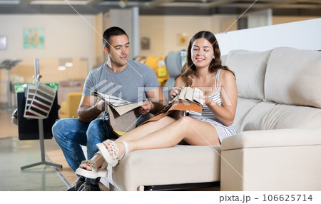 Cheerful couple choosing upholstery for lounge furniture in store 106625714