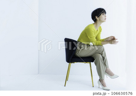 白背景の椅子に座る若い女性の全身のファッションポートレート 106630576