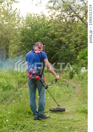 Worker mowing tall grass with electric or petrol lawn trimmer in the backyard. it doesn't work properly. 106632314