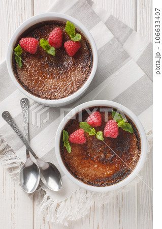 Spanish Chocolate creme brulee with caramelized sugar on top decorated with mint and raspberries close-up in a ramekin. Vertical top view Spanish Chocolate creme brulee with caramelized sugar on top decorated with mint and raspberries close-up in a ramekin. Vertical top view 106633407
