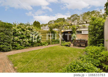 a backyard area with green grass and bushes in the foregrounded area, there is a small wooden bench on the right side a backyard area with green grass and bushes in the foregrounded area, there is a small wooden bench on the right side 106633763