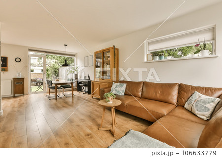 a living room with wood flooring and brown leather couches in the center of the room is an open kitchen, dining area 106633779