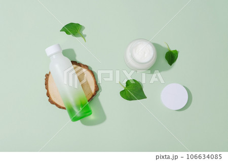 Top view of cosmetic bottle and jar mockup decorated with fish mint leaves and wooden podium on pastel background. Minimal concept for advertising. Using fish mint to treat acne is a safe and natural Top view of cosmetic bottle and jar mockup decorated with fish mint leaves and wooden podium on pastel background. Minimal concept for advertising. Using fish mint to treat acne is a safe and natural 106634085