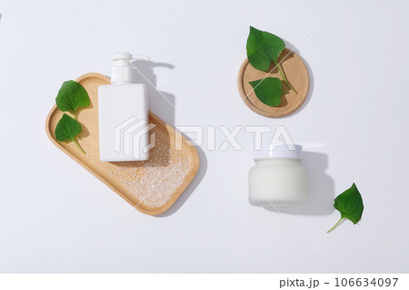 A pump bottle and cream jar unbranded displayed on wooden tray on white background with fresh fish mint leaves and bath salt. Fish mint has anti-inflammatory and antibacterial ingredients 106634097