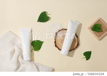Background for advertising cosmetics with minimal concept. A white plastic bottles unbranded arranged with fresh fist mint leaves, bath salt and a white cotton towel on a beige background Background for advertising cosmetics with minimal concept. A white plastic bottles unbranded arranged with fresh fist mint leaves, bath salt and a white cotton towel on a beige background 106634104