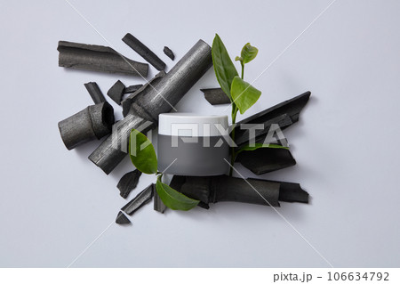Scene for advertising cosmetic with natural ingredients displayed on light gray background with mockup jar. Active ingredients found in bamboo charcoal and green tea are widely used in cosmetics Scene for advertising cosmetic with natural ingredients displayed on light gray background with mockup jar. Active ingredients found in bamboo charcoal and green tea are widely used in cosmetics 106634792