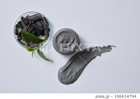 On the petri dish are bamboo charcoal and green tea bud decorated with a black jar container mask and streaks of mask substance on a light gray background. Top view, advertising photo On the petri dish are bamboo charcoal and green tea bud decorated with a black jar container mask and streaks of mask substance on a light gray background. Top view, advertising photo 106634794