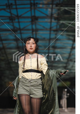 A beautiful Asian woman in shorts and a green leather coat comes out of the subway.  106635599