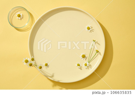 On the yellow background, a round plate decorated with chamomilla (Tanacetum parthenium). Minimal concept with copy space for cosmetic of chamomilla extract presentation 106635835