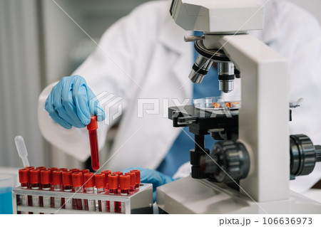 Doctor taking a blood sample tube from a rack with machines of analysis in the lab background, Technician holding blood tube test in the research laboratory. Doctor taking a blood sample tube from a rack with machines of analysis in the lab background, Technician holding blood tube test in the research laboratory. 106636973