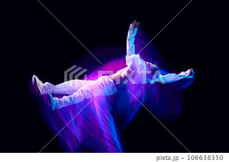 Freedom of movements. Young man in stylish clothes in motion against black studio background in neon with mixed lights effect 106638350