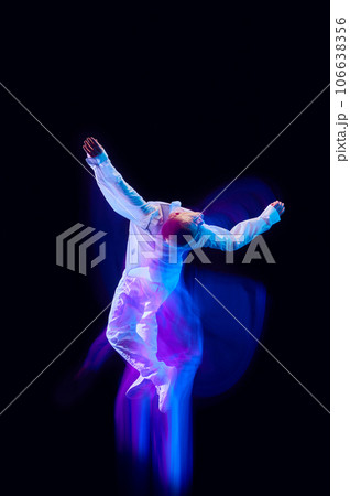 Freedom of movements. Young man in stylish clothes in motion against black studio background in neon with mixed lights effect 106638356