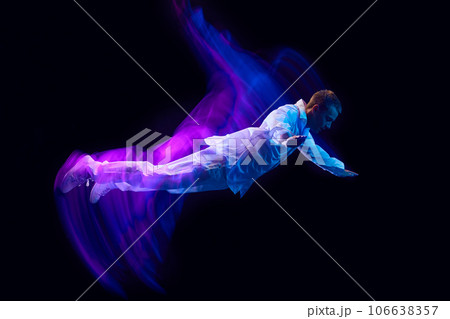 Freedom. Young guy in stylish clothes falling down against black studio background in neon with mixed lights effect. Levitation 106638357