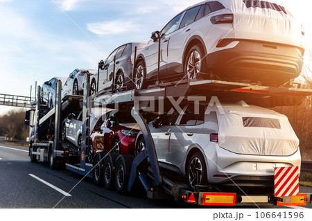 Tow truck car carrier semi trailer on highway carrying batch of new wrapped electric SUVs on motorway road at sunset evening time. Business distribution logistics service. Lorry driving highway 106641596
