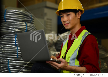 Asian male manager wearing hardhat using laptop and checking inventory in a warehouse Asian male manager wearing hardhat using laptop and checking inventory in a warehouse 106641838