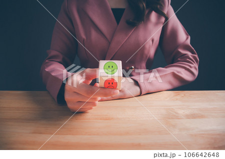Businesswoman choosing on the happy Smile face icon give satisfaction in good service, Smile face on wooden block cube for positive mindset selection. Mental health and emotional state. Hand focus. 106642648