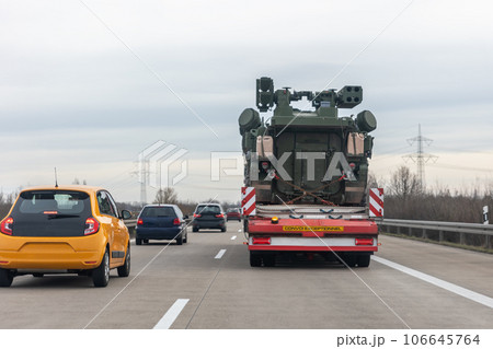 Back view armoured personnel carrier stryker with air defense system trailer hauler carrier truck drive military convoy highway road. US troops moving reloceation force reinforcement eastern Europe Back view armoured personnel carrier stryker with air defense system trailer hauler carrier truck drive military convoy highway road. US troops moving reloceation force reinforcement eastern Europe 106645764