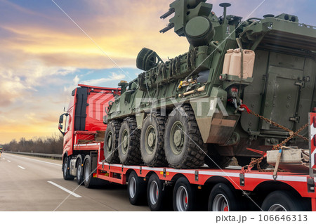 Back view armoured personnel carrier stryker with air defense system trailer hauler carrier truck drive military convoy highway road. US troops moving reloceation force reinforcement eastern Europe 106646313