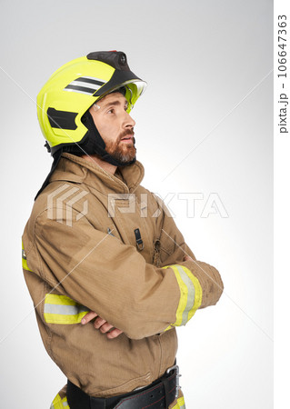 Strong, serious guy in fireman's uniform looking up and away in studio. Side view of firefighter waiting, with crossed hands, isolated on white background. Concept of work, firefighting, hope. Strong, serious guy in fireman's uniform looking up and away in studio. Side view of firefighter waiting, with crossed hands, isolated on white background. Concept of work, firefighting, hope. 106647363