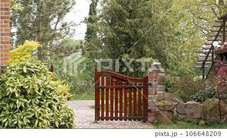 Beautiful brown wooden gates in a green garden, one part slightly open, inviting you inside 106648209