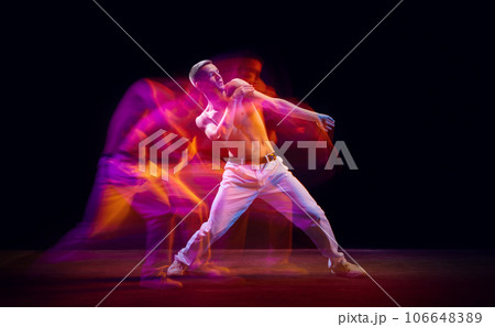 Inspiration and freedom. Young shirtless guy making chaotic movements against black studio background in neon with mixed lights effect Inspiration and freedom. Young shirtless guy making chaotic movements against black studio background in neon with mixed lights effect 106648389