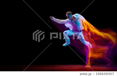 Aspiration. Young man in stylish clothes in motion, jumping against black studio background in neon with mixed lights effect Aspiration. Young man in stylish clothes in motion, jumping against black studio background in neon with mixed lights effect 106648407