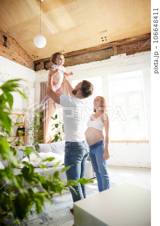 Happy caring parents, man and pregnant woman playing with little girl, daughter at home. Happy caring parents, man and pregnant woman playing with little girl, daughter at home. 106648411