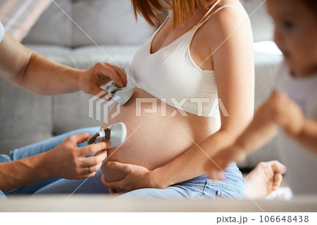 Happy family expecting baby. Cropped image of man and pregnant woman holding little baby shoes 106648438